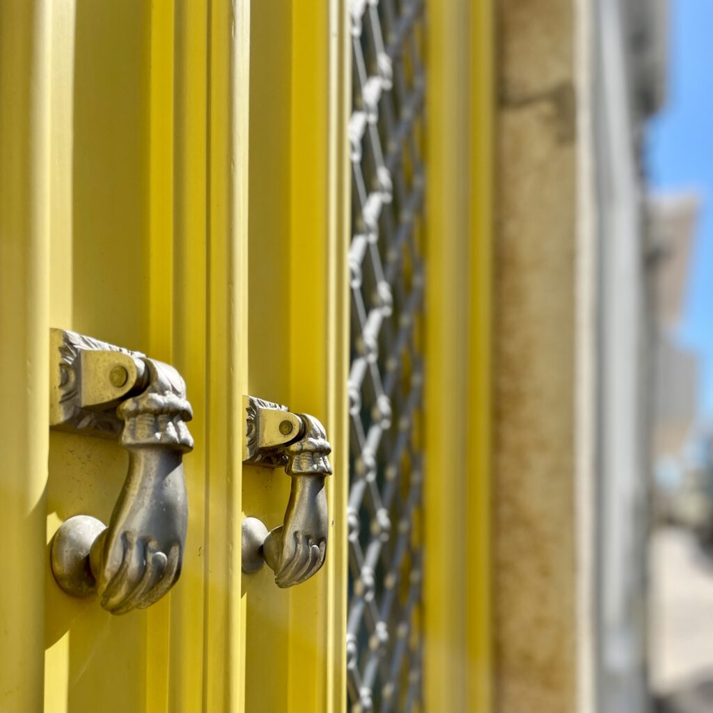 Bright yellow entrance door in Olhão with traditional hand-shaped doorknobs