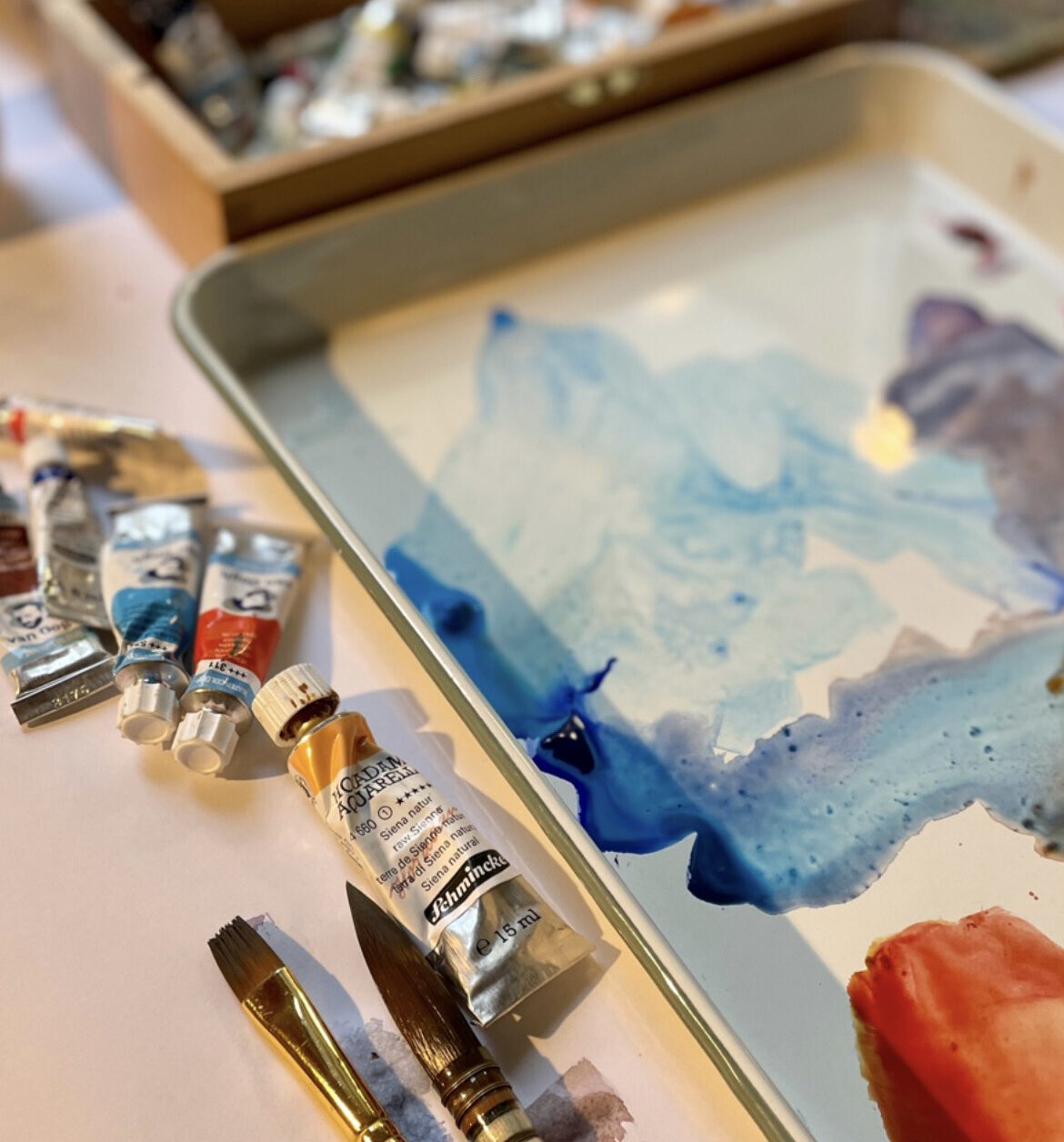 Close-up of a watercolor palette with half-mixed colours, showing the painting process for the Watercolour Winter Weekends course.