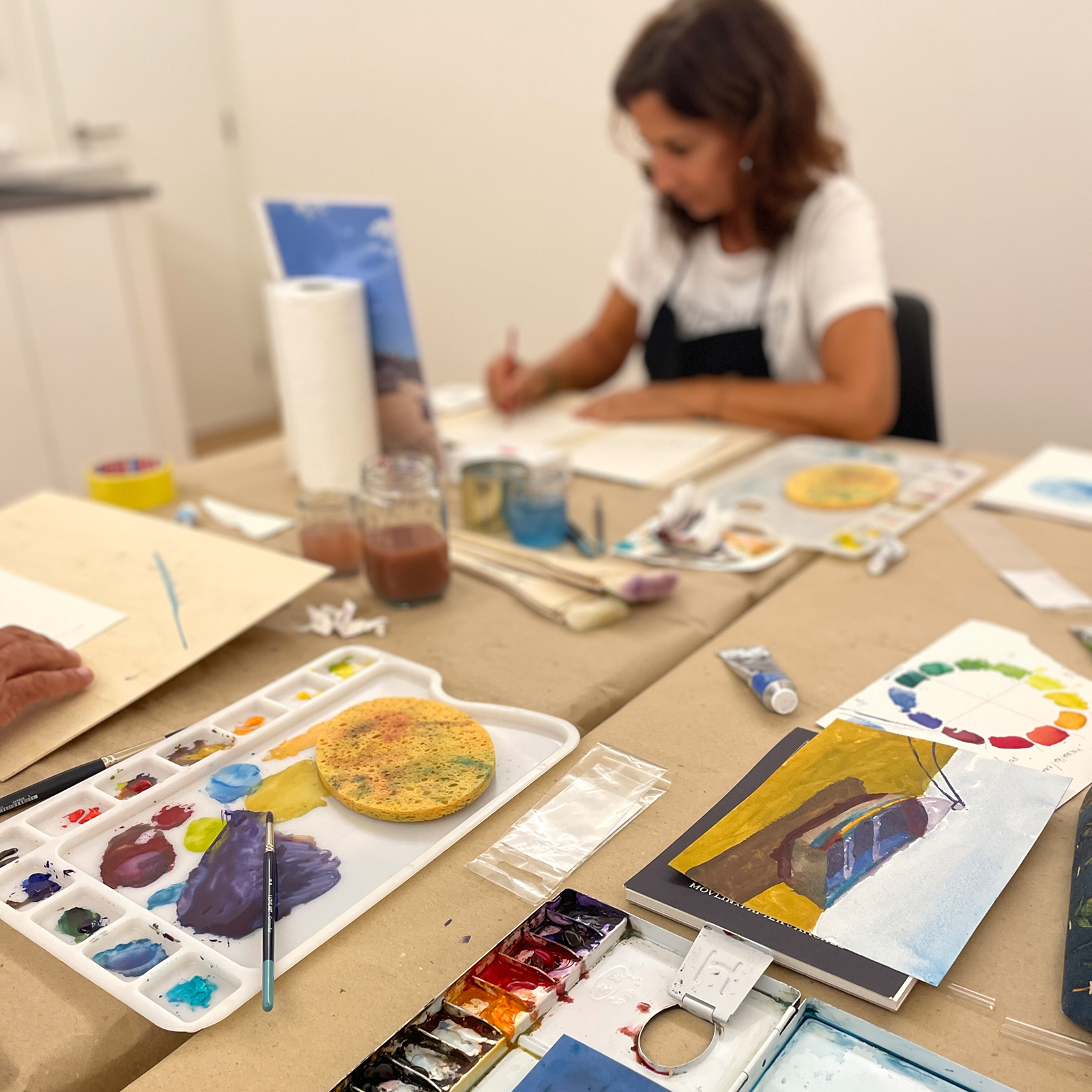 Woman painting during the “Barcas de Olhão” watercolor course, seated in the art space with a table full of watercolor supplies.