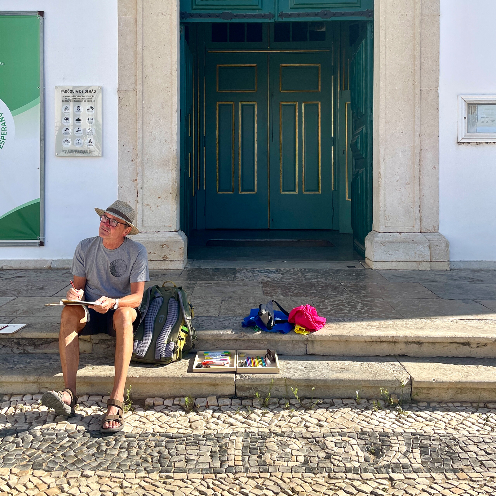 Man sitting on the steps of Igreja Matriz in Olhão, sketching in the early morning light.