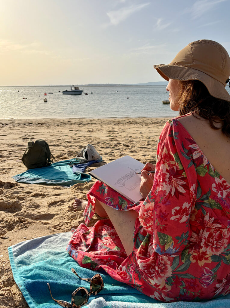 Participant observing Algarve light and sea reflections with a sketchbook during a plein-air art experience on Ilha do Farol